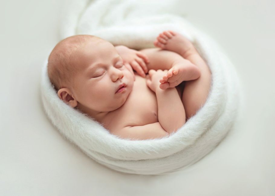 Baby schläft entspannt eingerollt in einem hellen Tuch