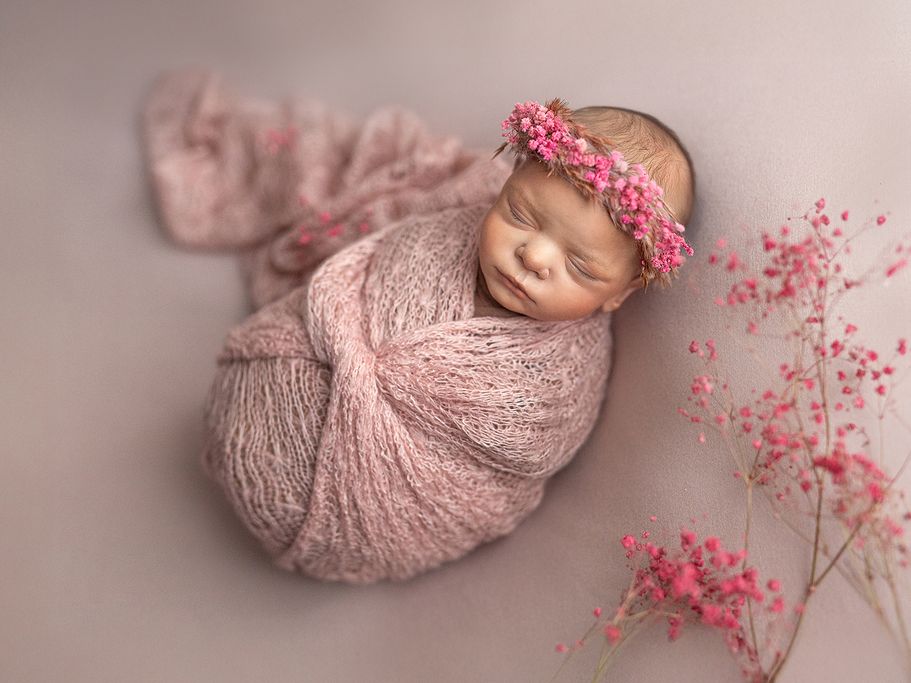Neugeborenes liegt auf rosa Decke – Fine-Art Newborn Fotografie Baby gepuckt mit Tuch warmem Licht mit getrockneten Blumen